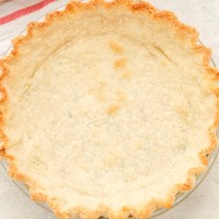 Overhead view of a blind baked pie crust next to a striped towel.