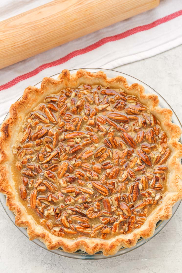 Overhead view of a pecan pie next to a rolling pin and a striped towel. 