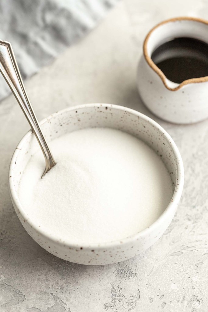 A bowl of granulated sugar next to a small jug of molasses. 