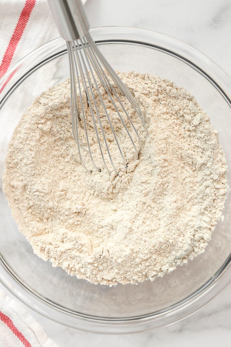 A glass bowl filled with the dry ingredients for a cake with a whisk on the side.
