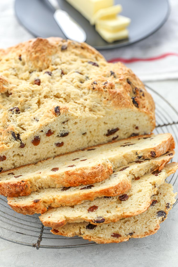 A sliced loaf of Irish Soda Bread on top of an antique round cooling rack with white and red napkin in the background. 