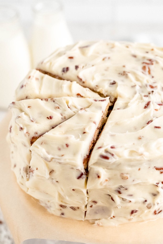 An Italian Cream Cake that's been sliced on a cake stand. Two milk jugs rest in the background.