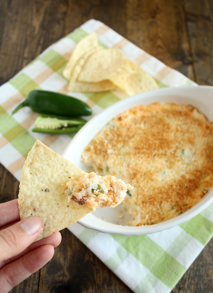 A chip has been scooped into a baking dish of jalapeno popper dip with bacon and is being held aloft. 