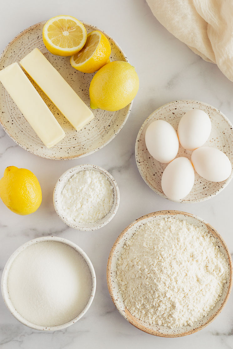 The ingredients for lemon bars in various bowls and plates on top of a marble surface.