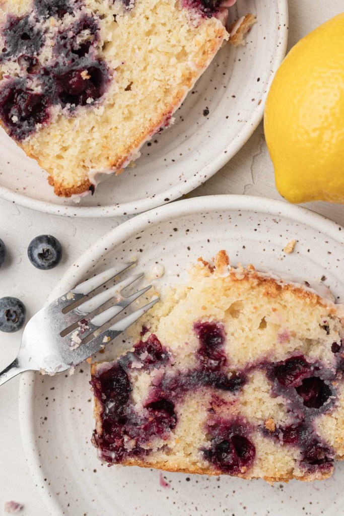 An overhead view of two slices of lemon blueberry quick bread on white speckled dessert plates. 