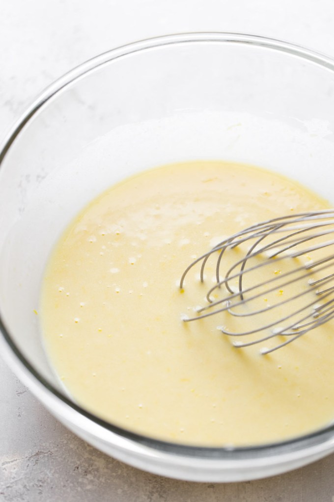 Wet ingredients and a whisk needed to make muffins in a glass mixing bowl.