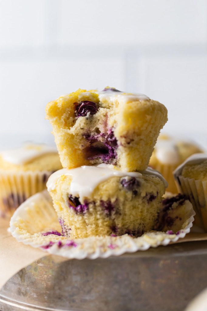 Lemon blueberry muffins on top of an overturned pie dish. The muffins in the front are stacked on top of each other and the top one has a bite taken out of it.