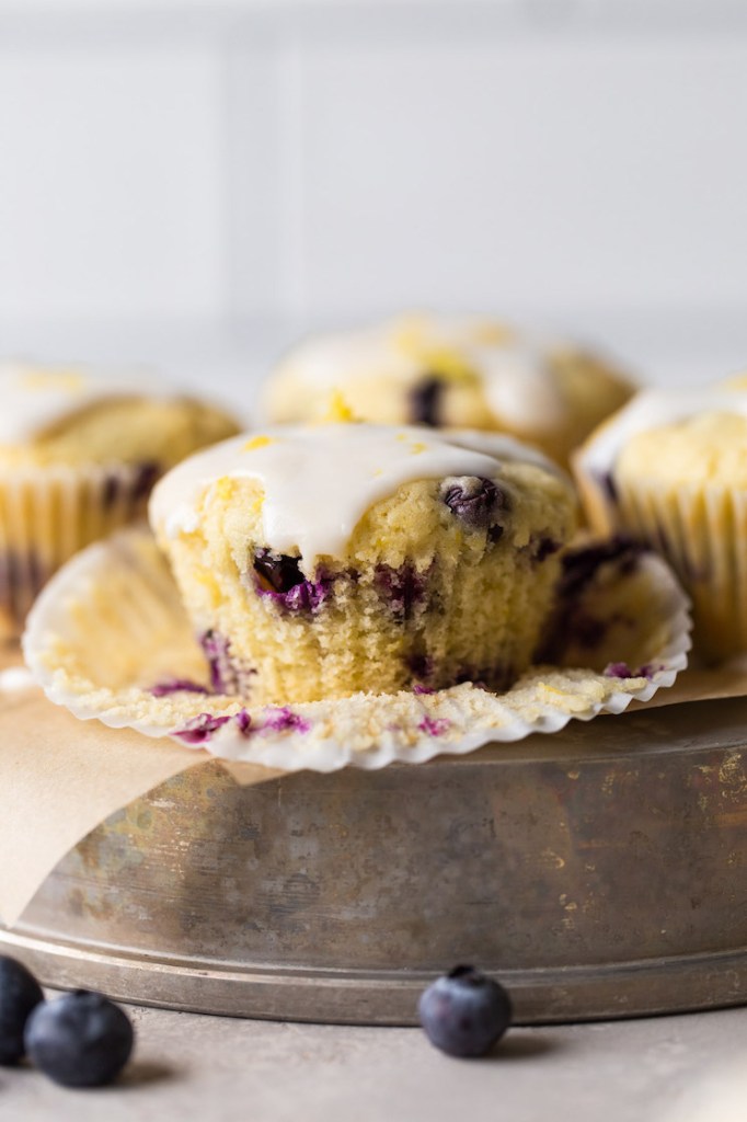 Four lemon blueberry muffins on an overturned cake tin, viewed from the side. 