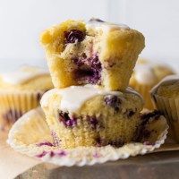 Lemon blueberry muffins on top of an overturned pie dish. The muffins in the front are stacked on top of each other and the top one has a bite taken out of it.