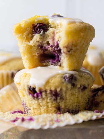 Lemon blueberry muffins on top of an overturned pie dish. The muffins in the front are stacked on top of each other and the top one has a bite taken out of it.