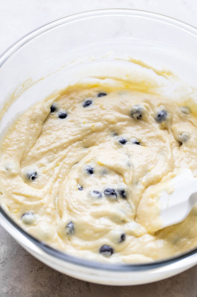 Lemon blueberry muffin batter in a glass mixing bowl. A rubber spatula rests in the bowl. 