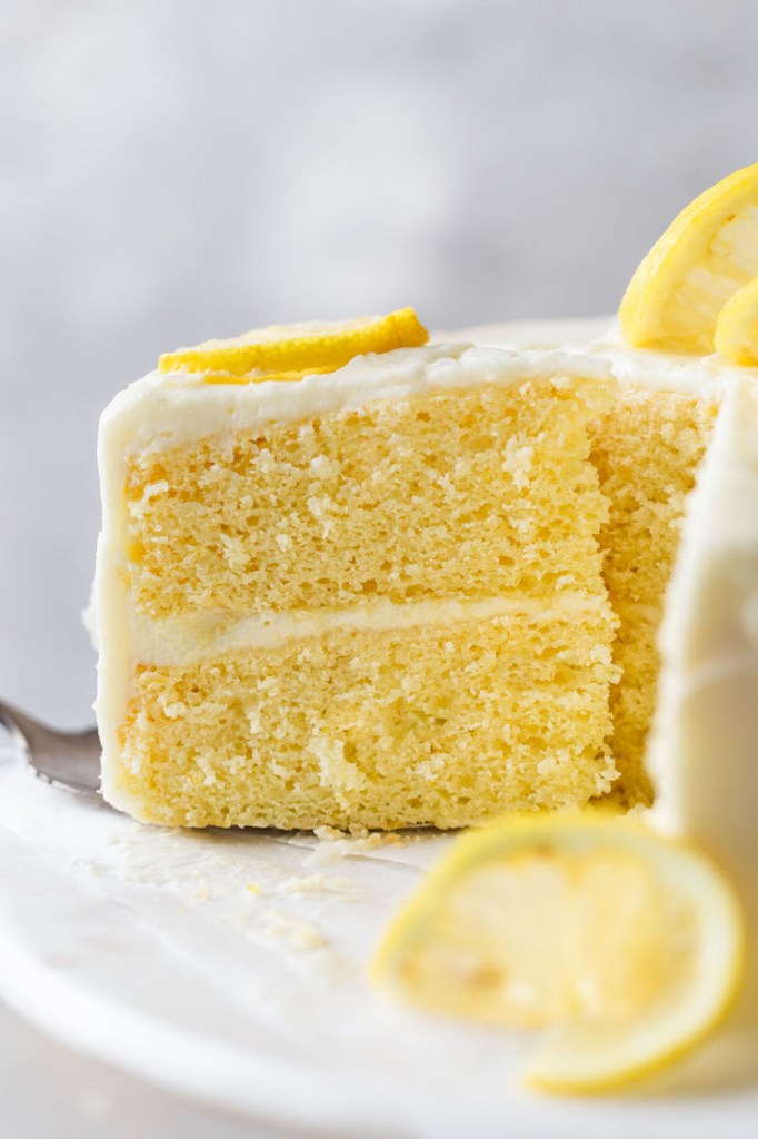 A side view of a slice of lemon cake being removed from a cake stand. 
