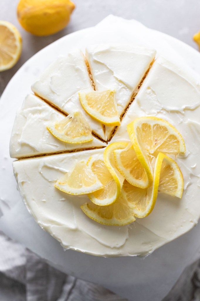 An overhead view of a lemon layer cake on a cake stand. Three slices have been cut but not yet removed from the cake. 