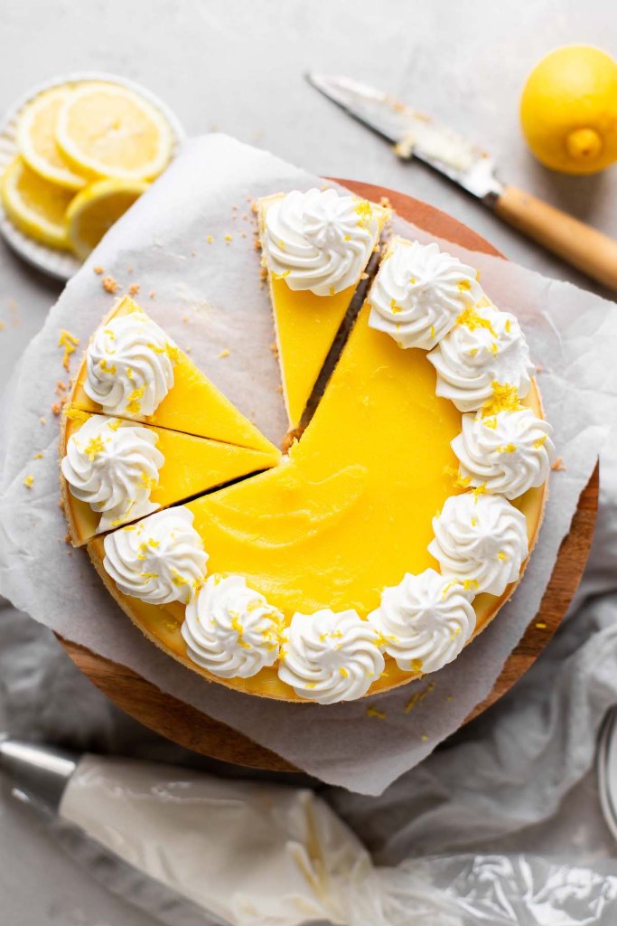 An overhead view of a lemon cheesecake on a cake stand. A few slices have been cut and one is missing. 