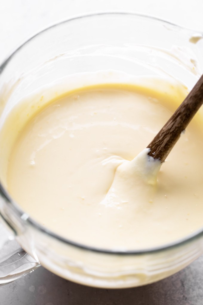 An overhead view of a glass mixing bowl filled with cheesecake filling.