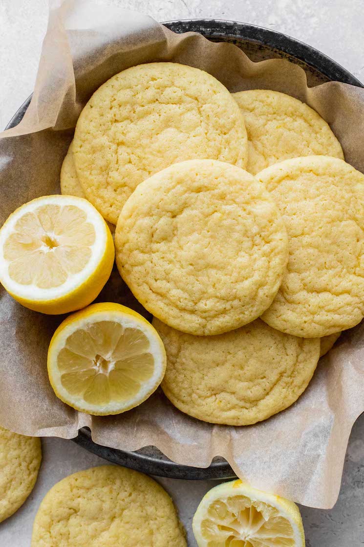 A round pan holding baked lemon cookies with a lemon cut in half beside them.