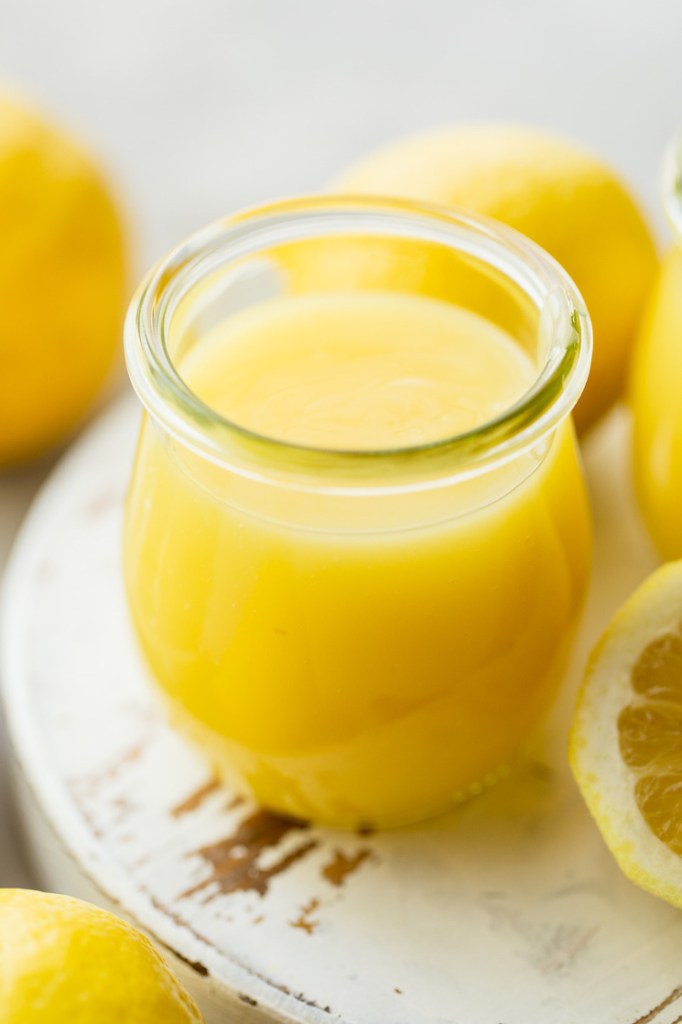 A small glass jar filled with microwave lemon curd sitting on top of a worn white wood surface.