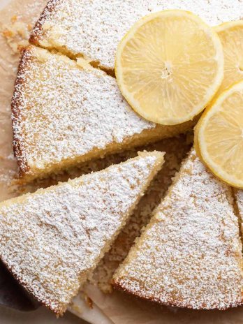 A sliced lemon olive oil cake on a piece of parchment paper. Once slice is being removed.