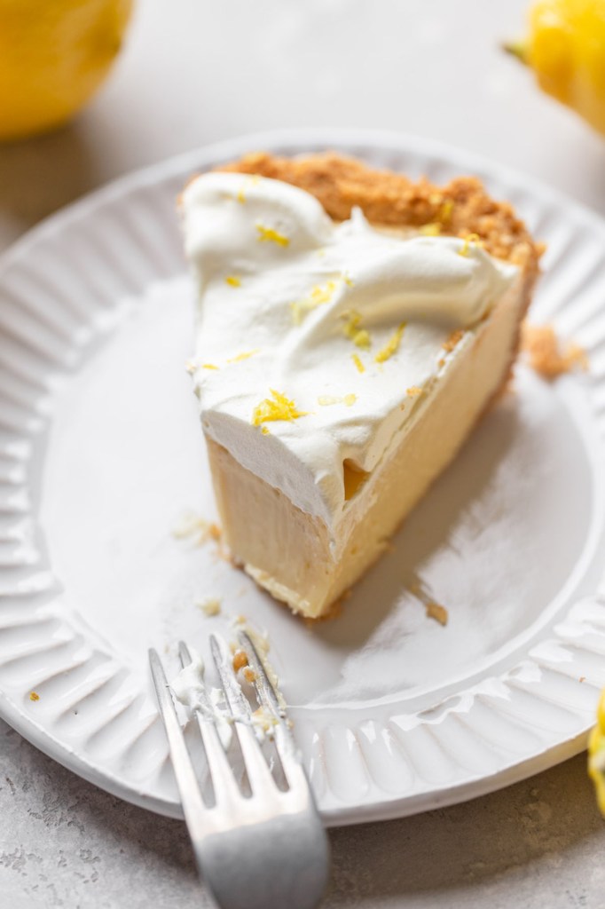 A single slice of lemon pie on a white plate with a bite taken out.