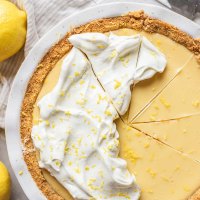A lemon pie in a white baking dish tipped with whipped cream and lemon zest.