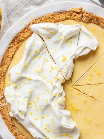 A lemon pie in a white baking dish tipped with whipped cream and lemon zest.