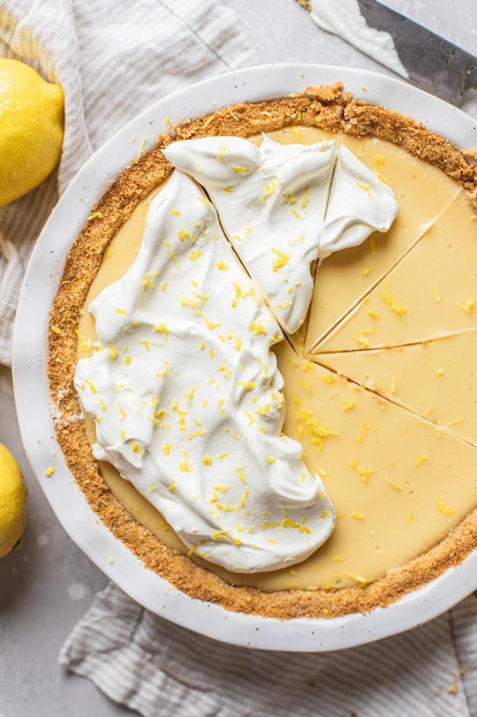 A lemon pie in a white baking dish topped with whipped cream and lemon zest.