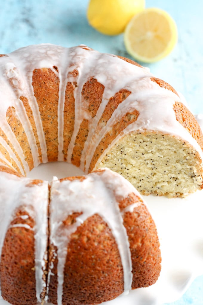 A glazed lemon bundt cake on a white cake stand. A slice has been removed. 