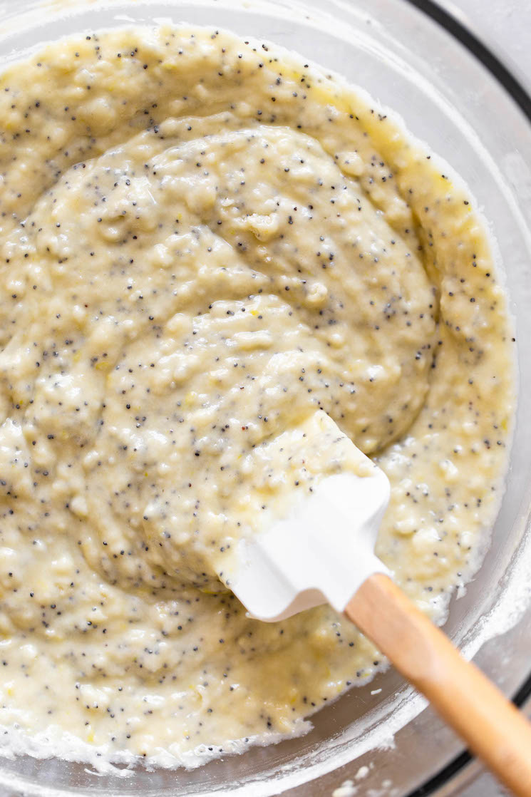 A glass bowl holding lemon poppy seed muffin batter being mixed with a rubber spatula.