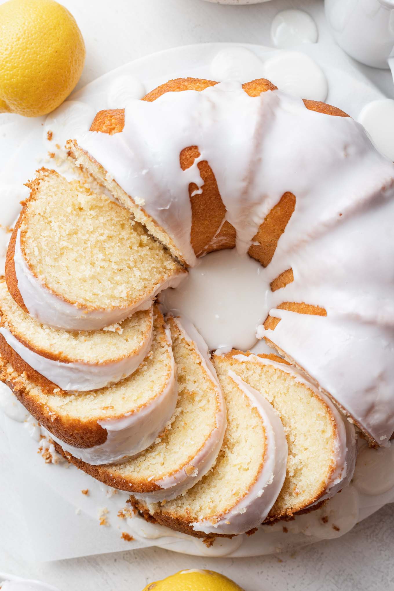 An overhead view of a lemon sour cream pound cake. Half the cake has been sliced, and the slices are laying on their sides. 