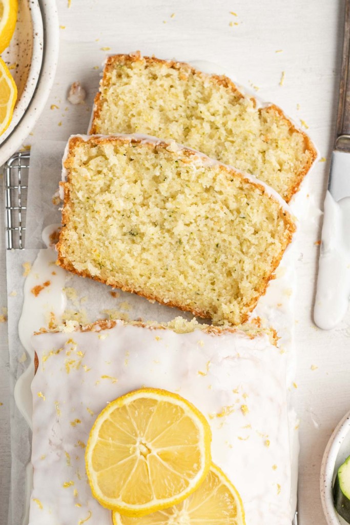 An overhead view of two slices of zucchini lemon bread lying on their sides next to the loaf.