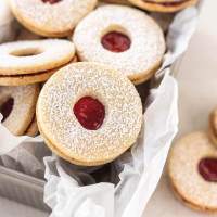 Several Linzer cookies in a loaf pan that's lined with parchment paper.