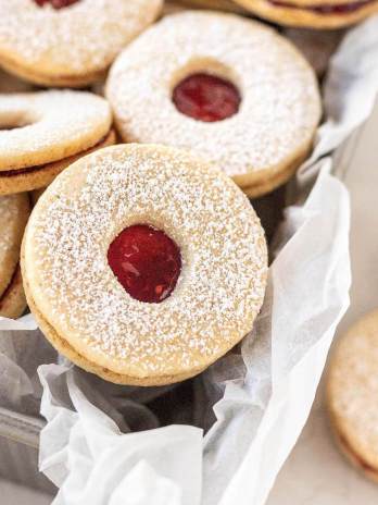 Several Linzer cookies in a loaf pan that's lined with parchment paper.