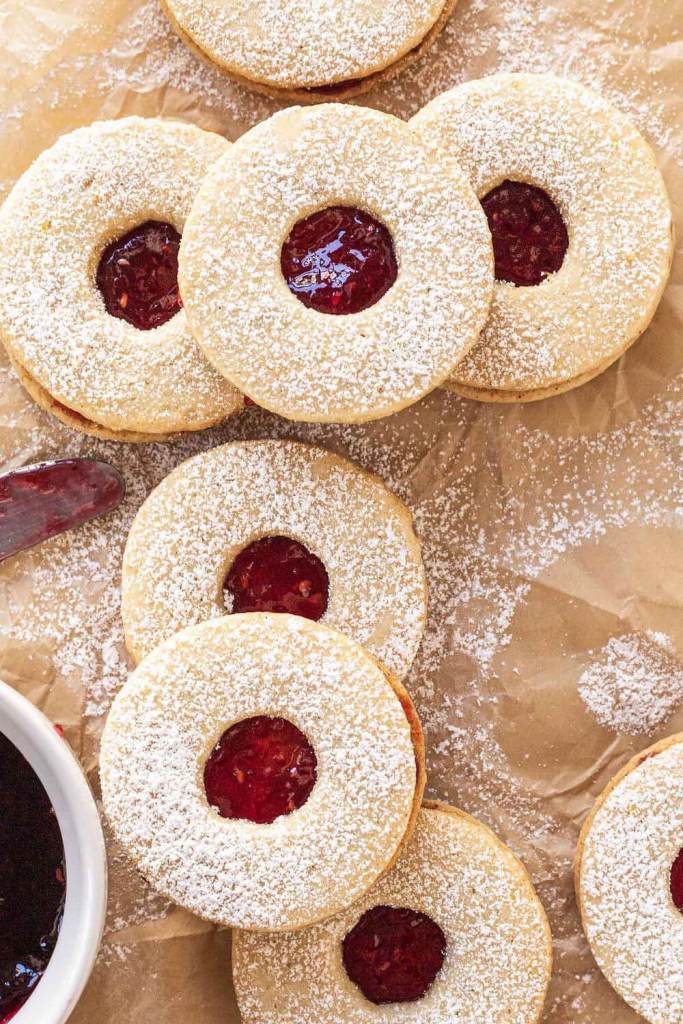 An overhead view of a pile of raspberry linzer cookies dusted with powdered sugar. 