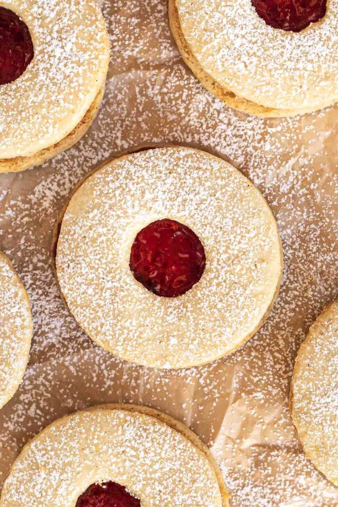 A close up, overhead view of Linzer cookies dusted with powdered sugar on parchment paper.