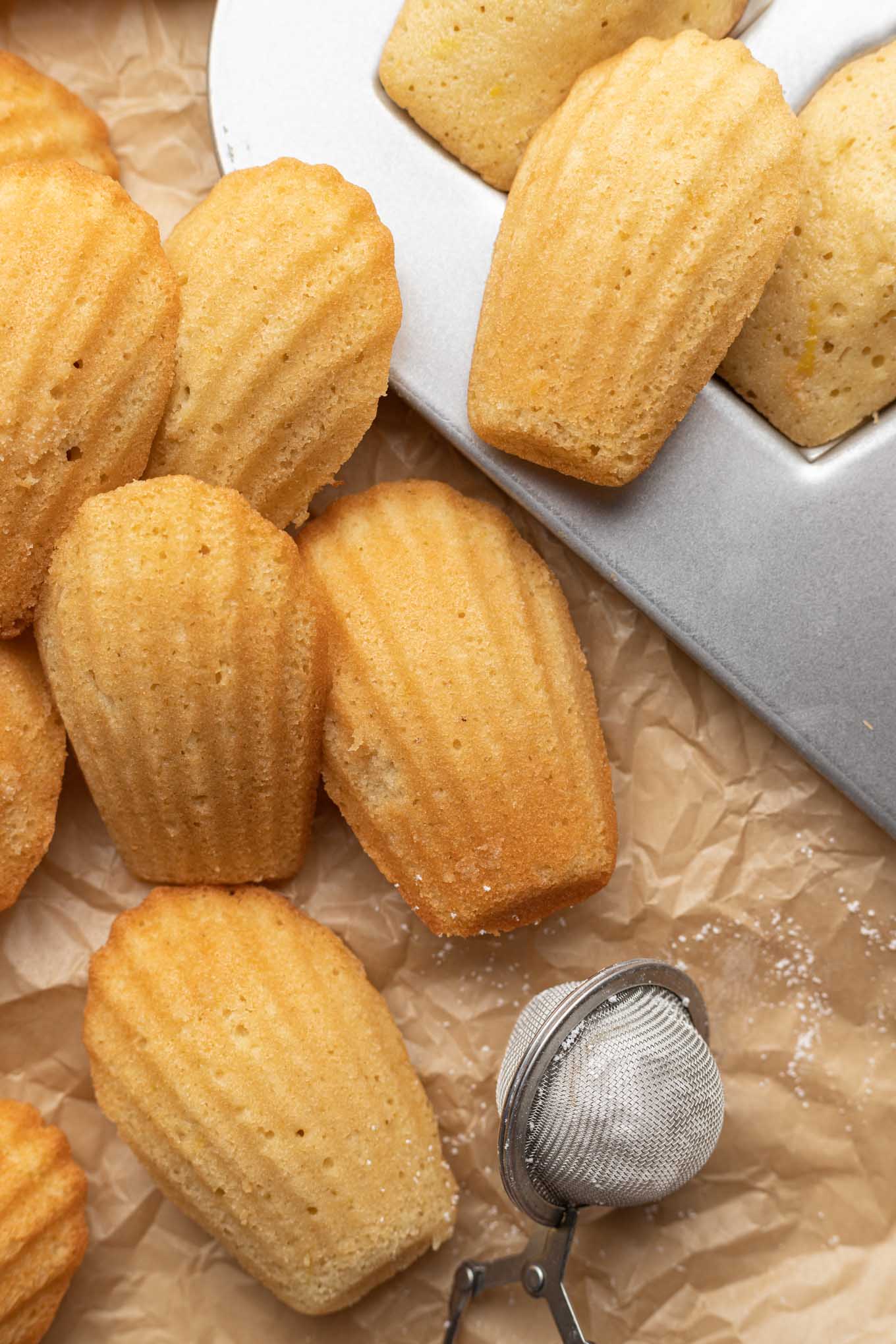 French madeleines piled next to a baking pan. 