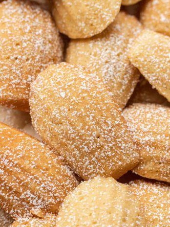 Several madeleine cookies dusted with powdered sugar on a piece of brown parchment paper.