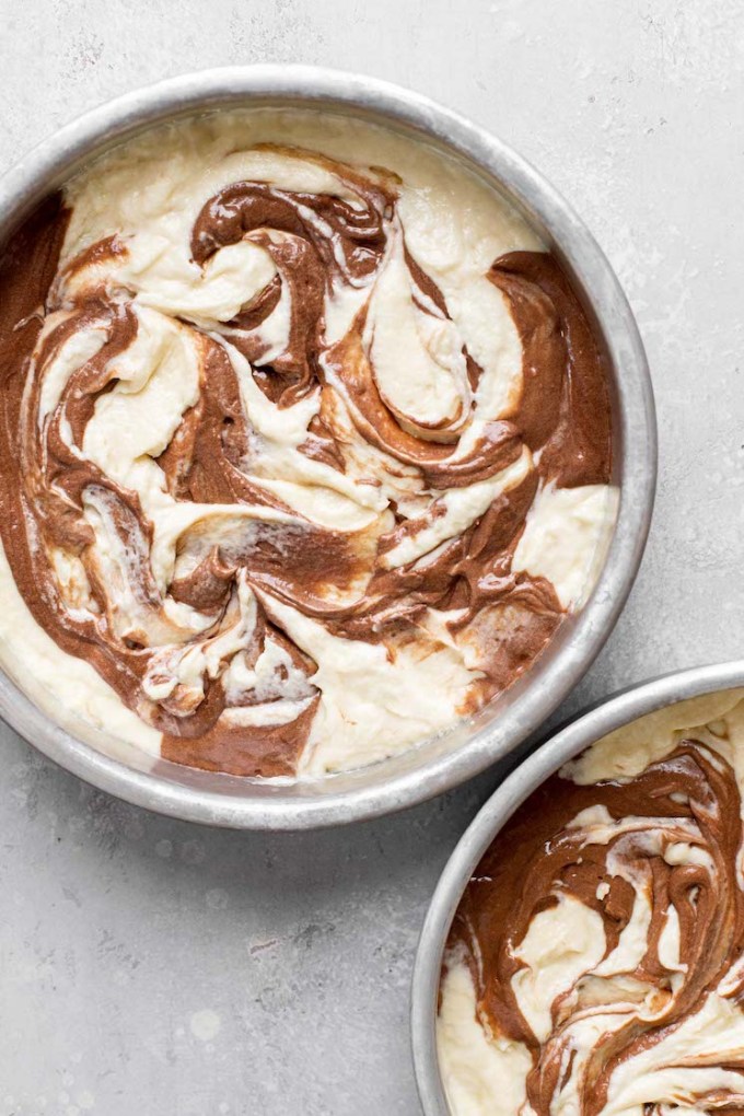 An overhead view of swirled marble cake batter in two cake pans, ready to be baked.