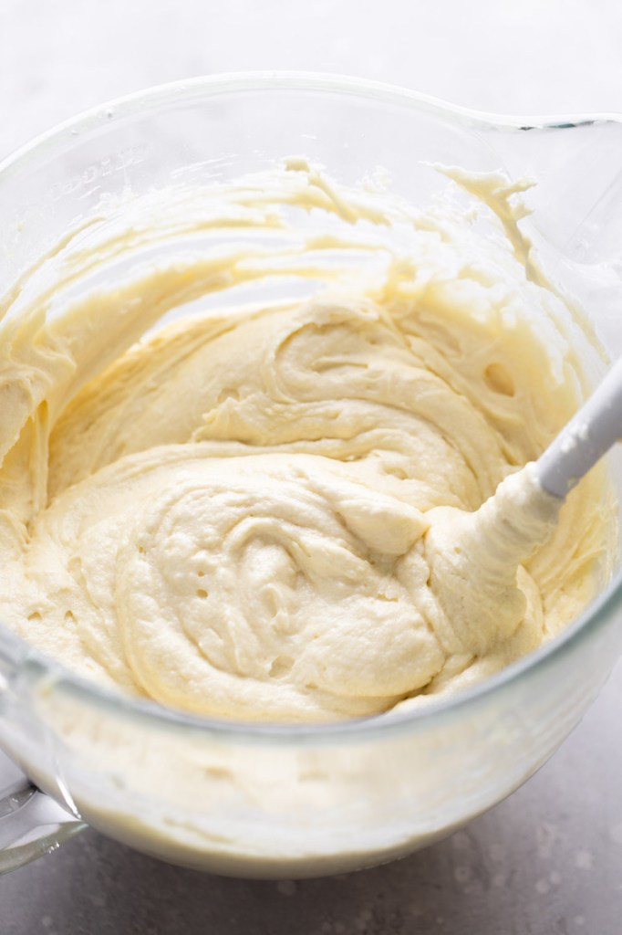 Vanilla cake batter in a glass mixing bowl with a rubber spatula. 