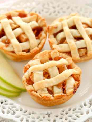 Three mini apple pies on a decorative white plate.