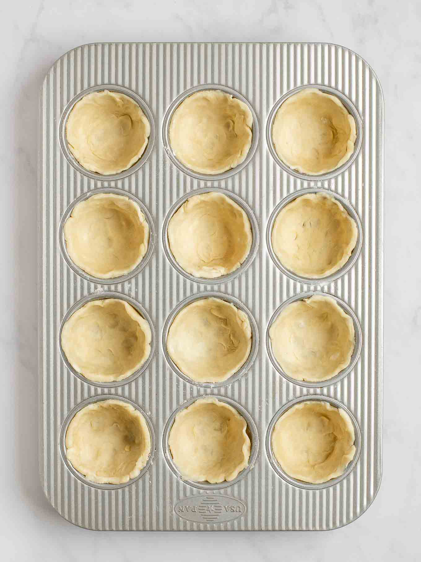 An overhead view of pie crust circles pressed into the cavities of a muffin pan.