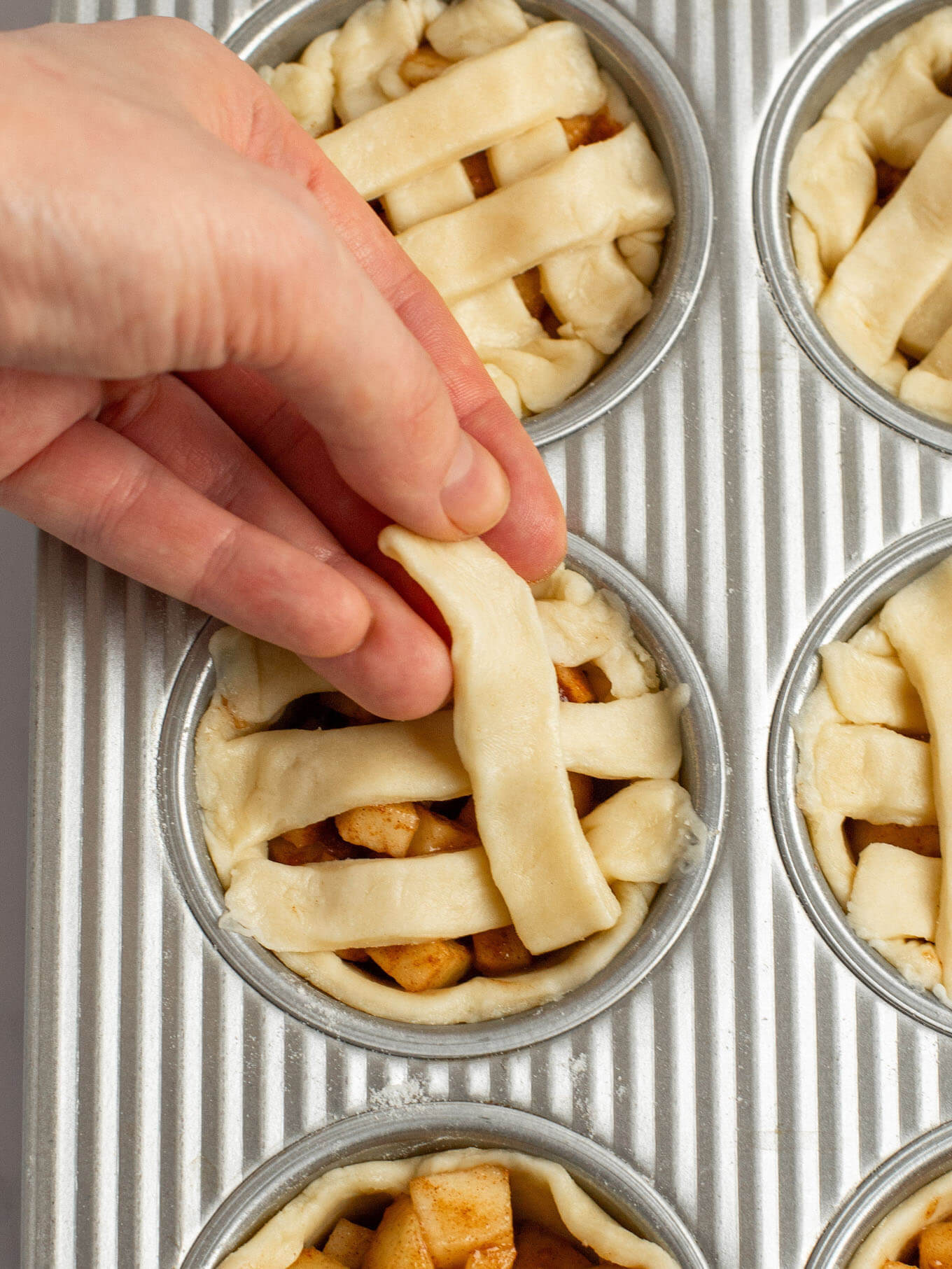 An angled view of small strips of pie crust being placed on top of the pies to create a lattice pie crust.