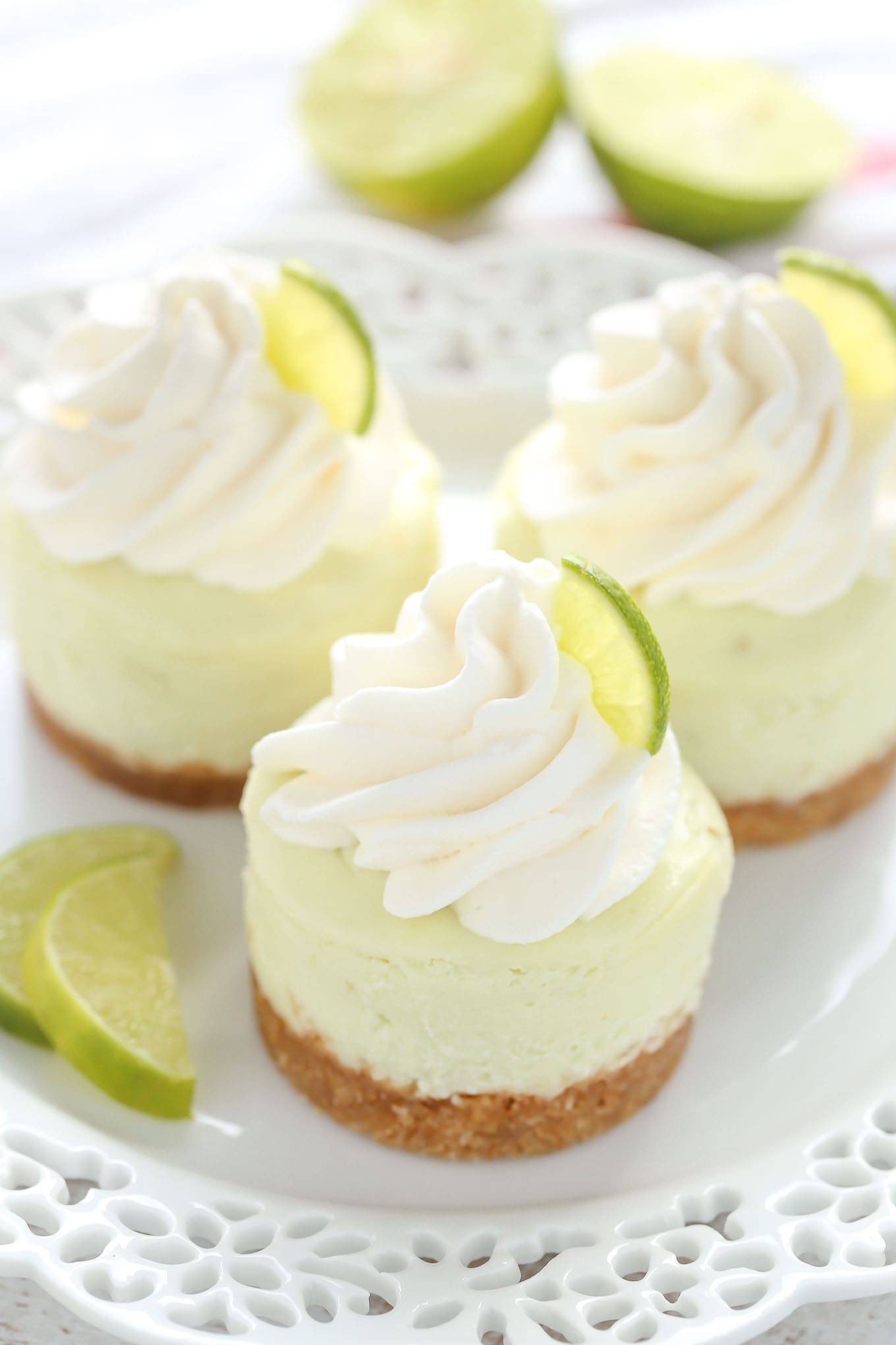 Three mini key lime cheesecakes on a white plate. Two lime halves are in the background. 