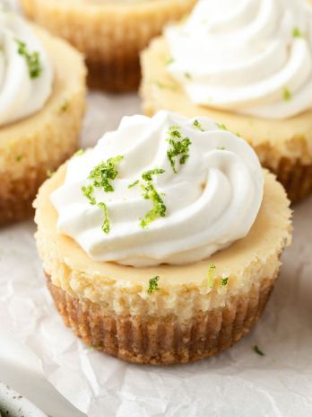 Mini key lime pies on a piece of parchment paper. Each mini pie is topped with whipped cream and a little lime zest.