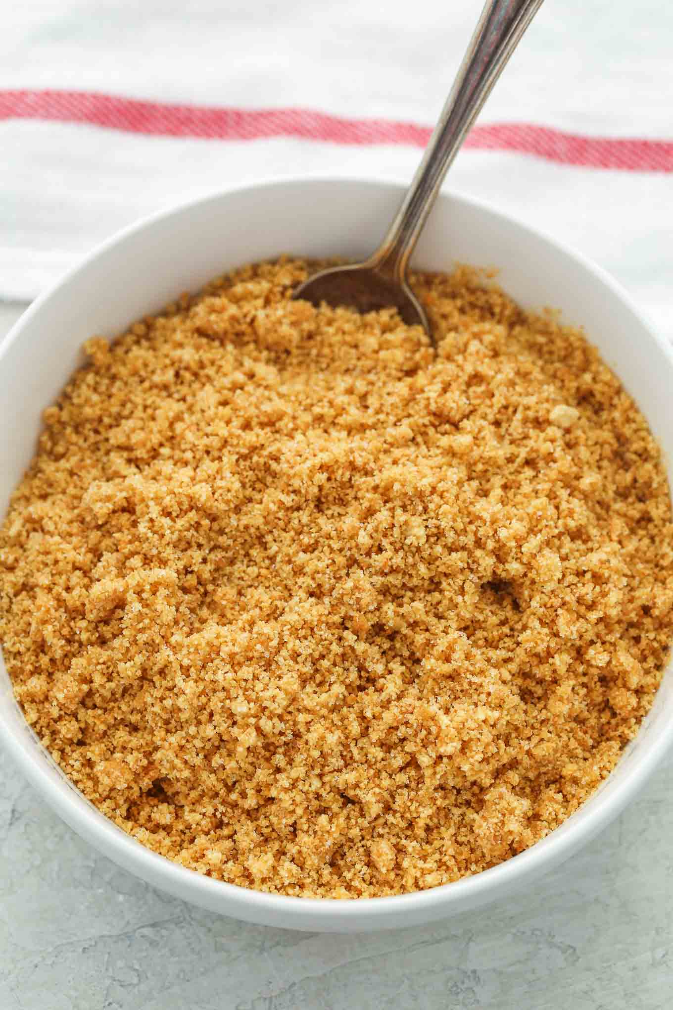 Overhead view of graham crackers crumbs in a white bowl with a spoon sticking out. 