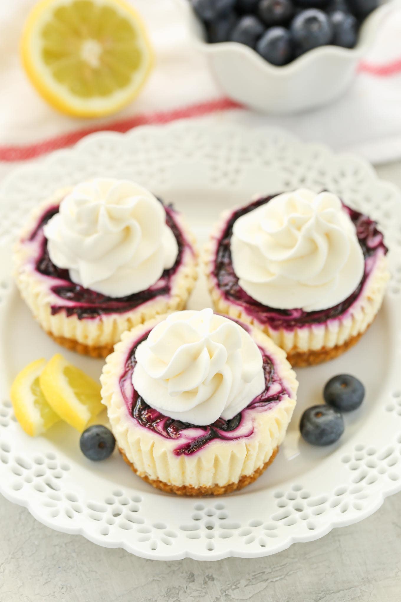 Three mini lemon blueberry cheesecake bites topped with whipped cream on a white plate. 