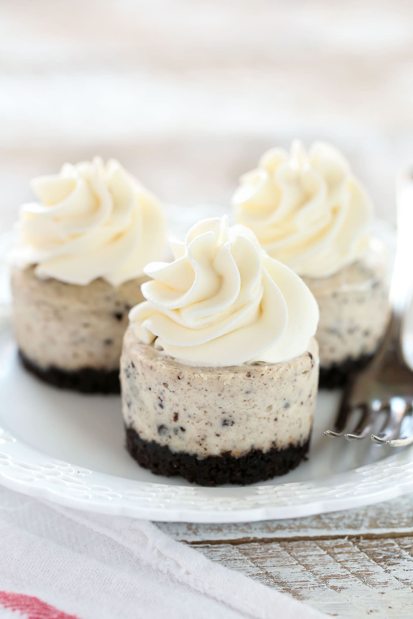 Three oreo cheesecake cupcakes on a white plate with a fork. 