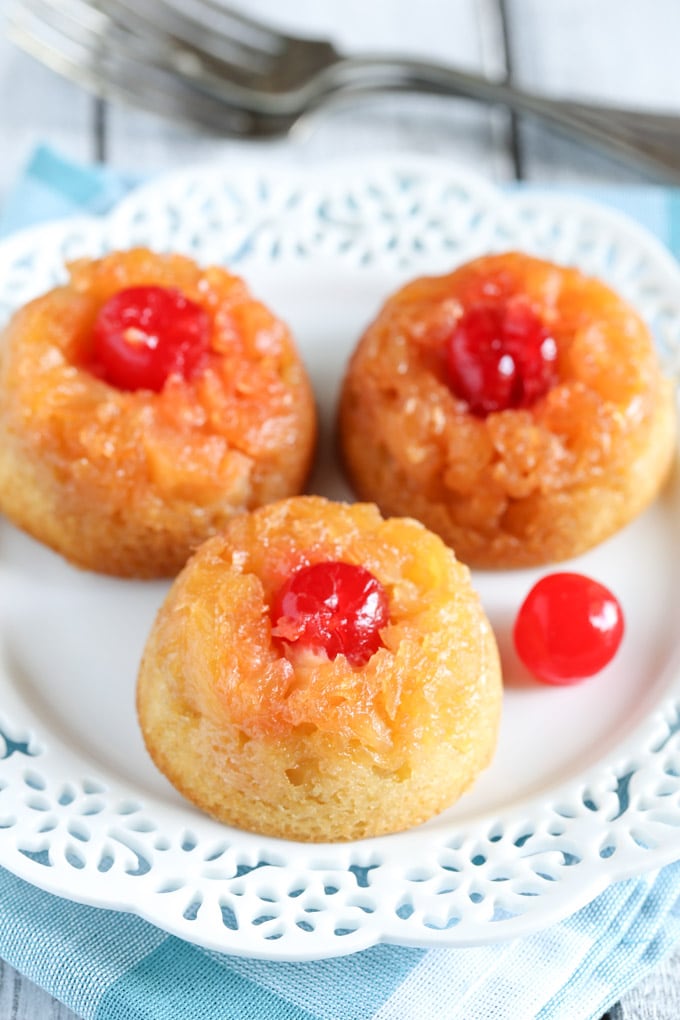 Three mini pineapple upside down cakes on a white dessert plate. A fork rests in the background. 