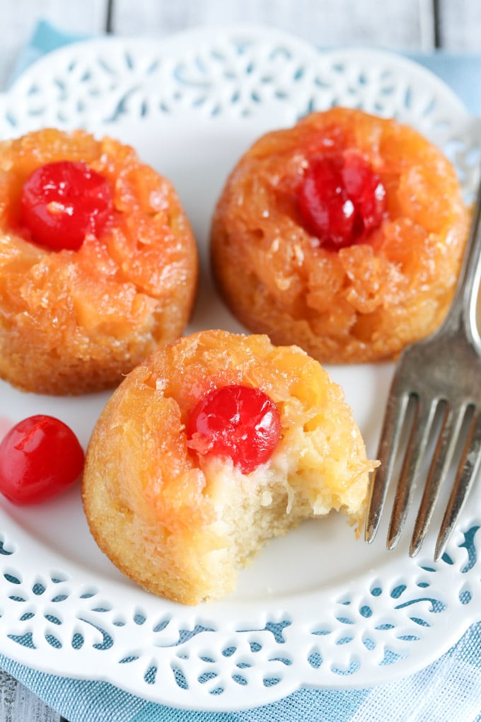 Three individual pineapple upside down cakes on a white plate with a fork. One mini cake has a bite missing.