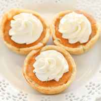 Three mini pumpkin pies topped with whipped cream on a decorative white plate.