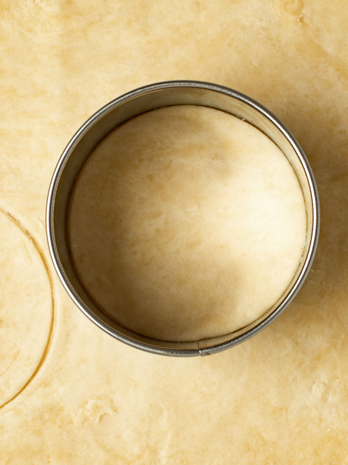 An overhead view of a pie crust that's been rolled out. A circular cookie cutter is cutting out a piece of the crust.
